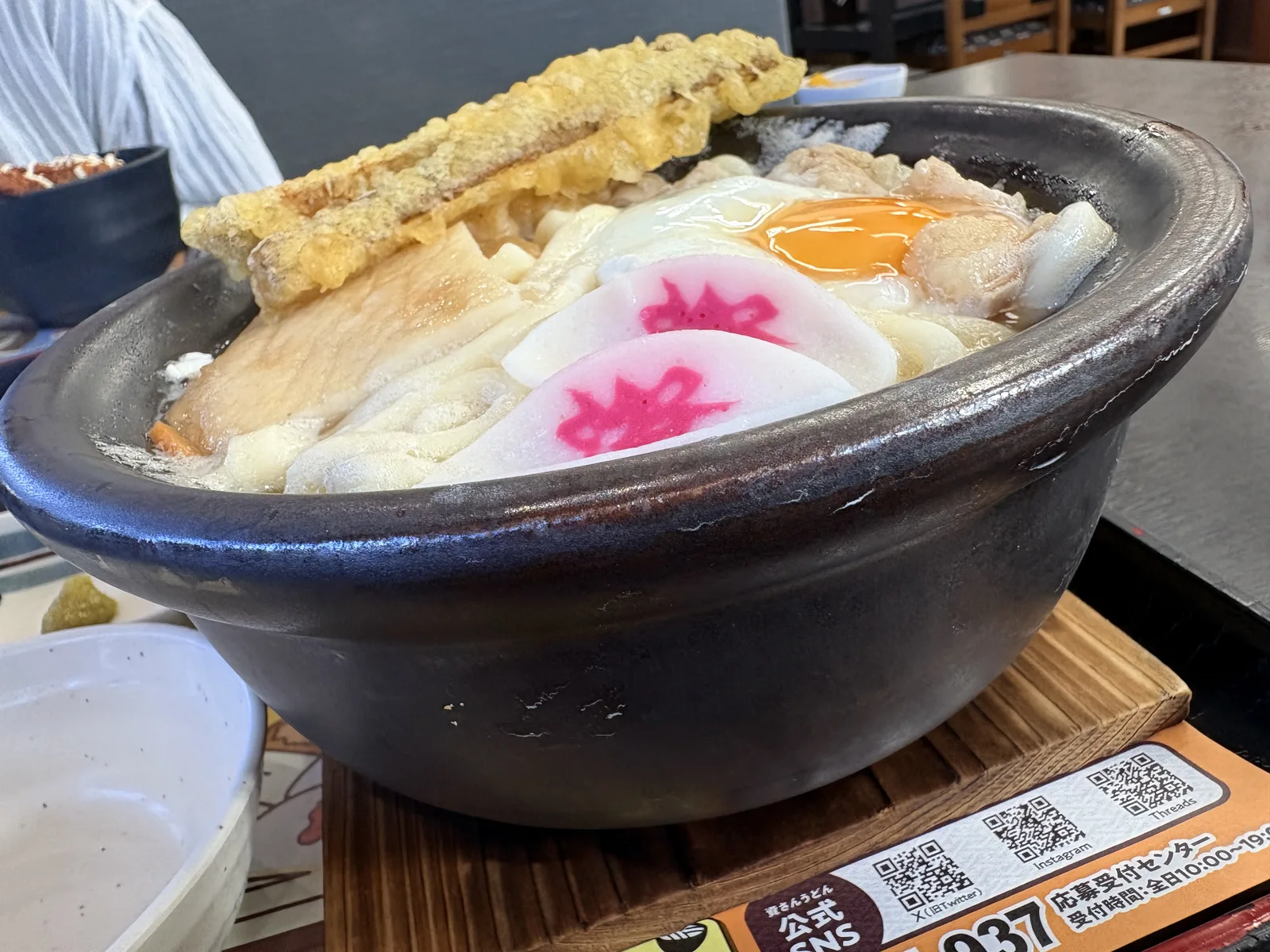 木の鍋敷きにのった土鍋を真横から。ごぼう天が土鍋からはみ出している