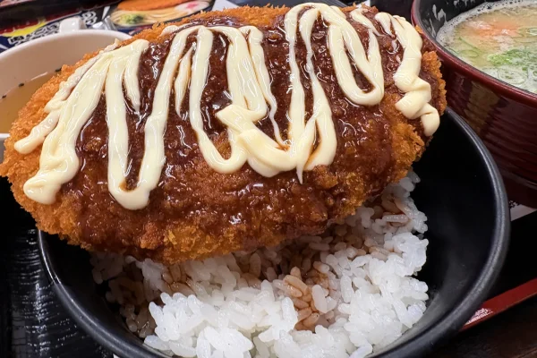 大判コロッケにソースとマヨネーズをたっぷりかけた「ソースコロッケ丼」。奥に豚汁