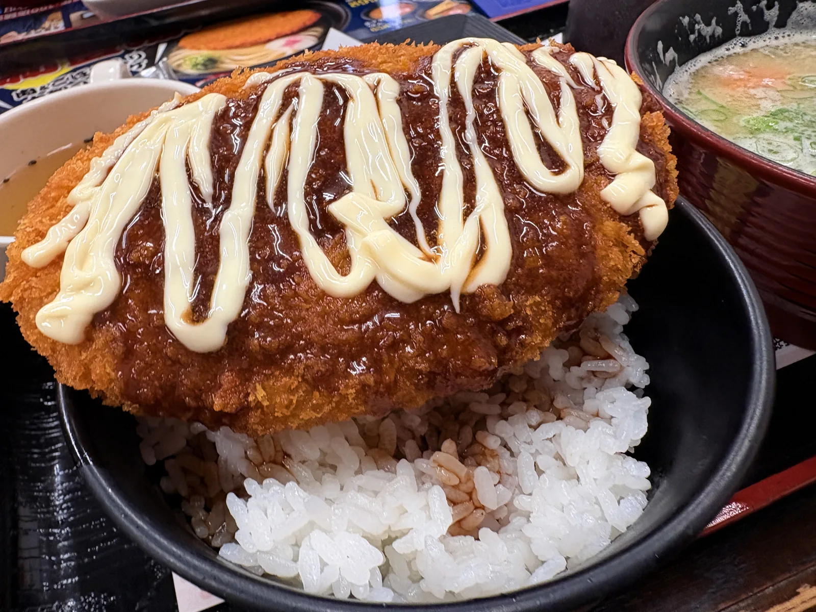 大判コロッケにソースとマヨネーズをたっぷりかけた「ソースコロッケ丼」。奥に豚汁