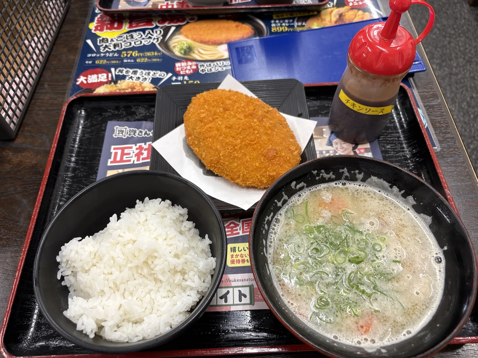 トレーに白ごはん、別皿の大判コロッケ、豚汁。右にソースのボトル