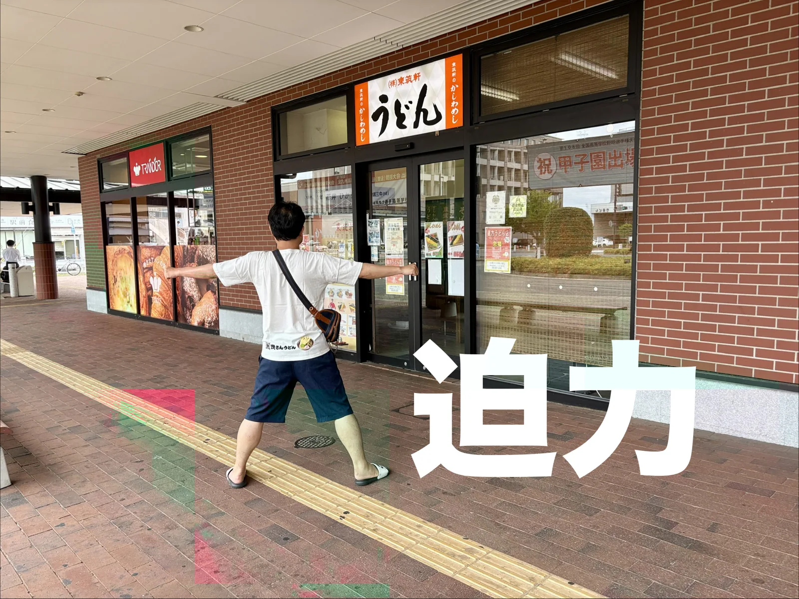 直方の店の前で迫力ポーズ。レンガの壁に「うどん」の看板