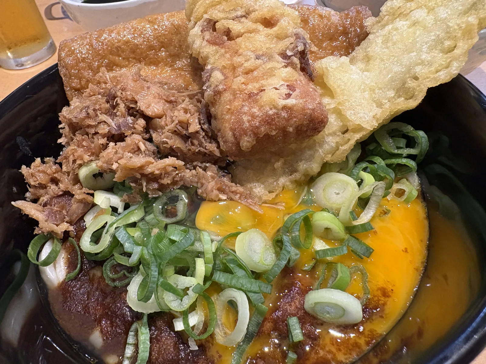 ほぼ全部のせカレーうどん。黒い器にお揚げ、かしわ、天ぷら、生卵、ねぎが山盛り