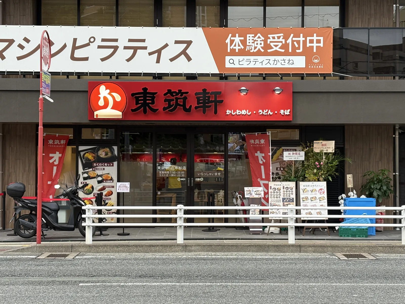東筑軒 六本松店の外観。2階にピラティスの横断幕、1階に赤い「東筑軒」の看板と開店祝いの花