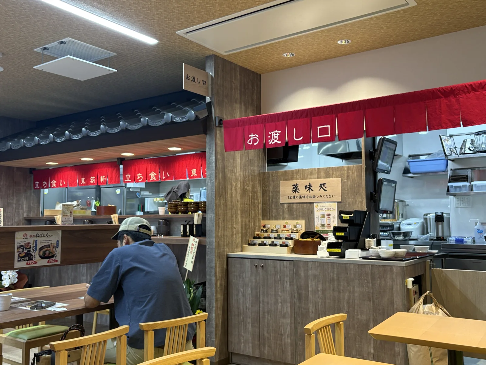 店内の様子。瓦屋根風の造作に「立ち食い 東筑軒」の赤いのれん、右手に「お渡し口」と薬味処