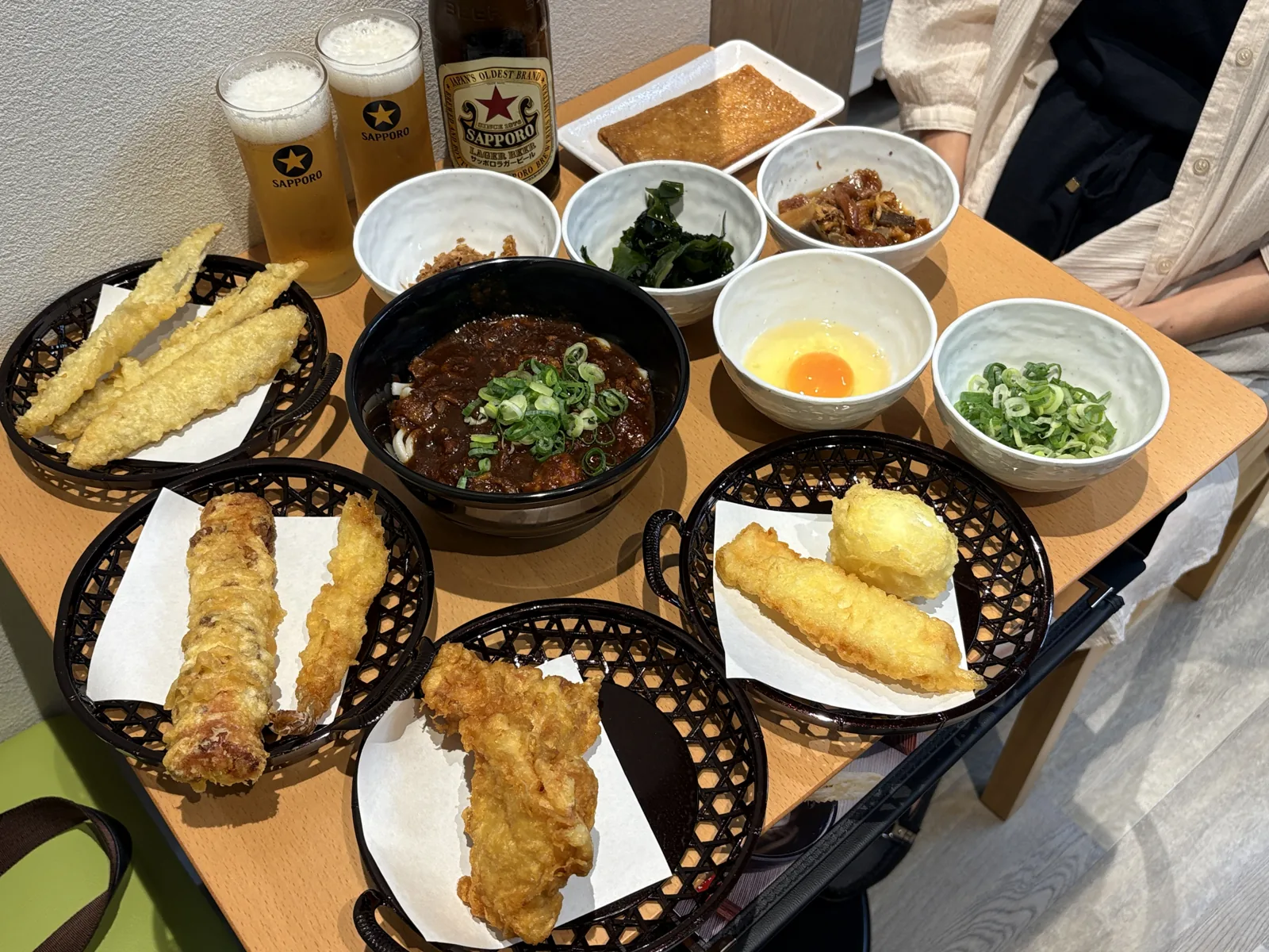 テーブルいっぱいに並んだカレーうどん、天ぷらのかご4つ、小鉢のトッピング、赤星