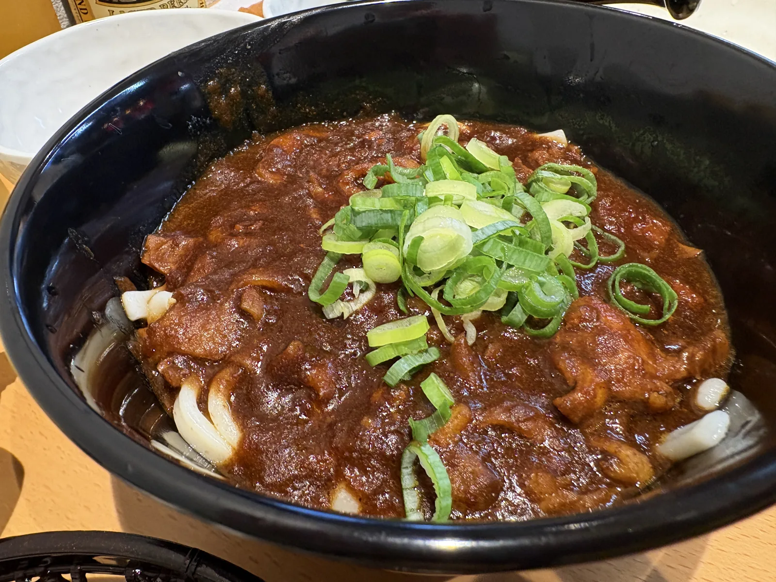カレーうどん。黒い器にとろみのあるカレーがたっぷり、真ん中にねぎ