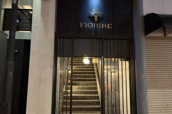 黒い壁に金色の花のロゴと「FIORIRE」の文字。格子の奥にランプに照らされた階段が続く