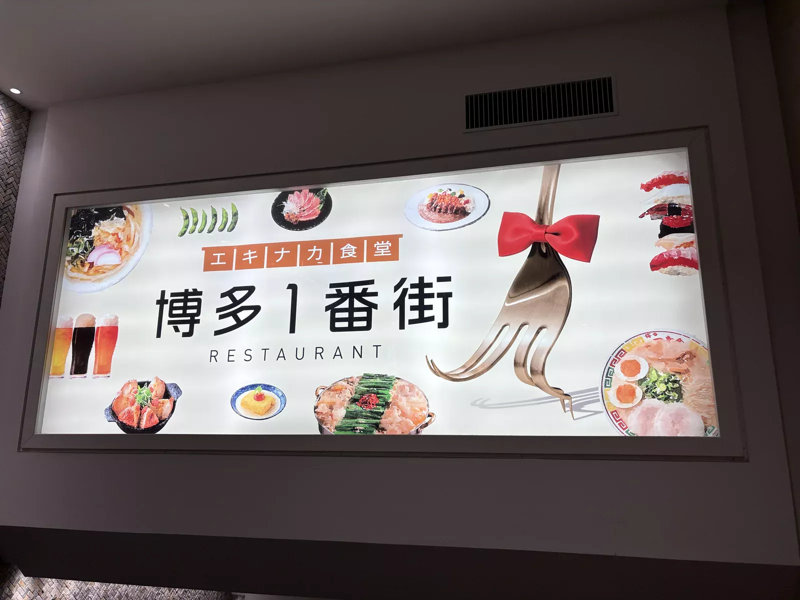 博多1番街の看板。「エキナカ食堂 博多1番街 RESTAURANT」の文字と、もつ鍋・ラーメン・寿司などの料理写真
