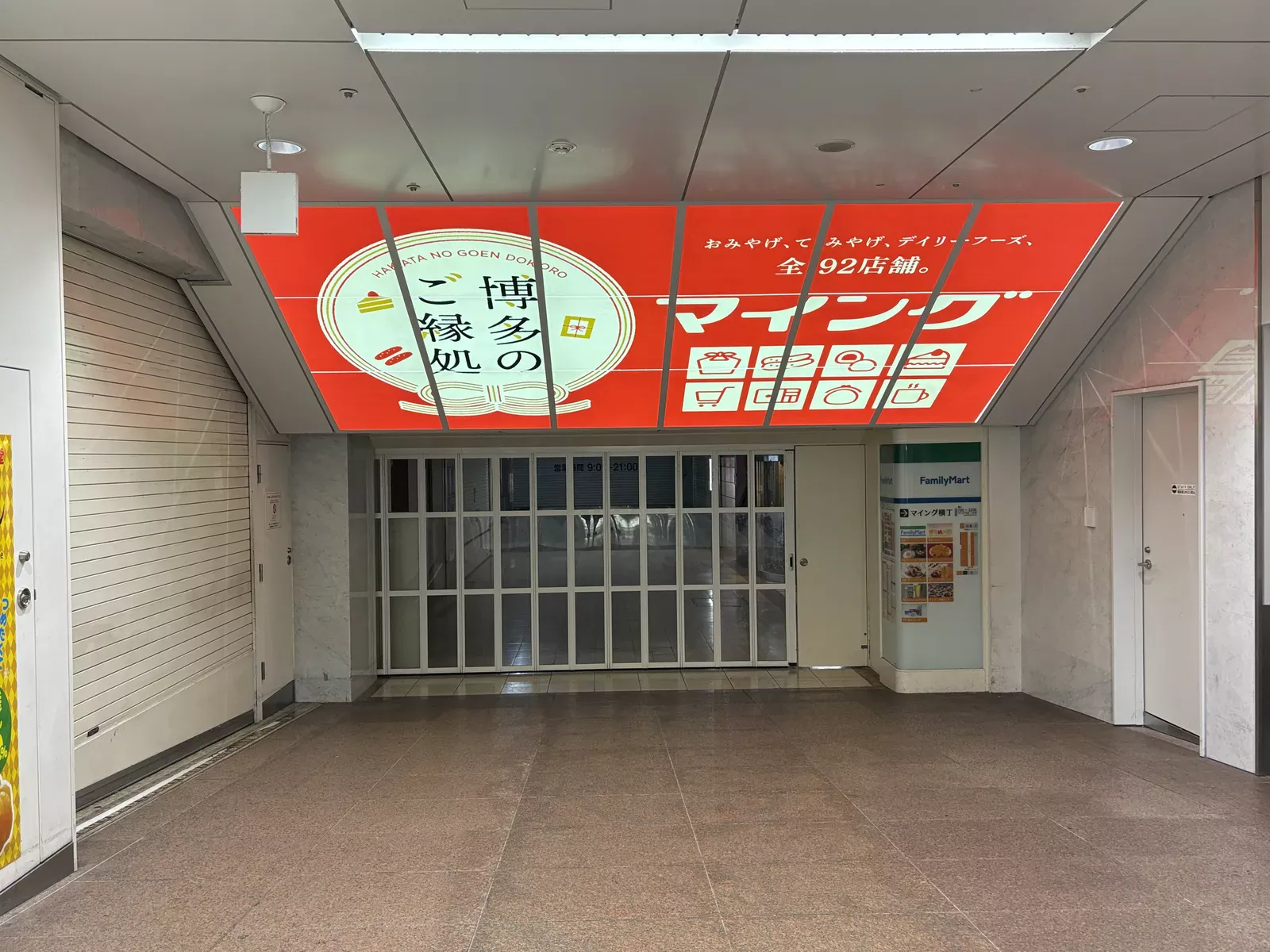 マイング奥の入口。「おみやげ、てみやげ、デイリーフーズ、全92店舗。」の大きな看板の下で、折れ戸が閉まっている