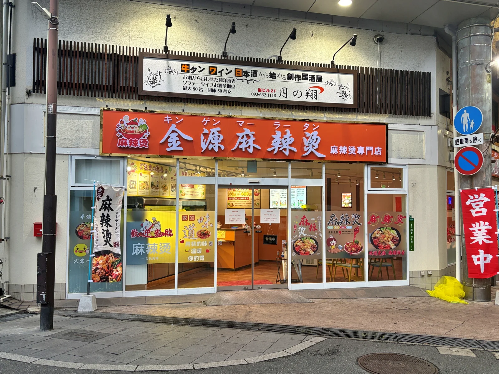 金源麻辣湯の外観。オレンジの看板に「金源麻辣湯（キンゲンマーラータン）麻辣湯専門店」、店先に「営業中」ののぼり