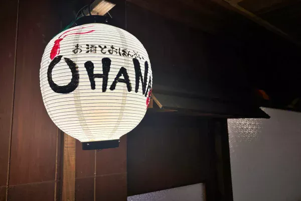 白い提灯に「お酒とおばんざい OHANA」の手書き文字。木の壁に灯りがともる