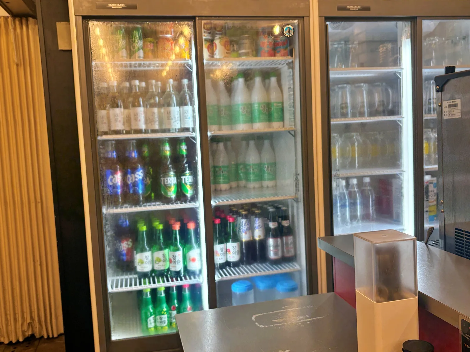 冷蔵庫に並ぶ韓国の瓶ビールCASS・TERRA、緑の瓶の韓国焼酎、マッコリのボトル