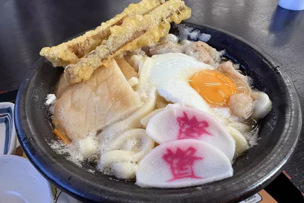 土鍋のもつ鍋うどん。ごぼう天2本、半熟の卵、「資」のかまぼこ2枚、もつがのる