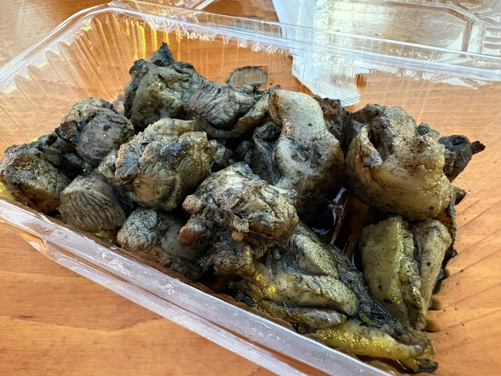 炭火家の地鶏の炭火焼き。炭で黒く焼き色のついた地鶏がパックに盛られている