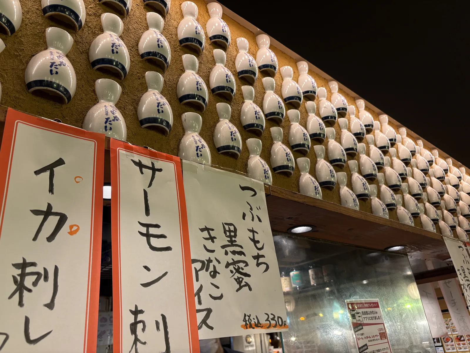 壁一面に「立ち呑み酒場 よかたい」の文字入りとっくりが埋め込まれている